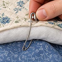 Using a curved safety pin to go through quilting to hold them together.