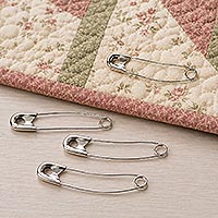 Several curved safety pins resting beside a quilted fabric project, demonstrating their use for holding quilt layers together during quilting.