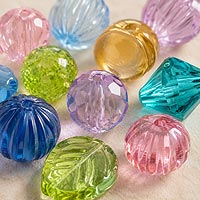 Close-up of assorted translucent craft beads in different shapes and colors, including faceted, round, ribbed, leaf, and bicone styles, showcasing their clear finishes and light-catching sparkle on a neutral background.